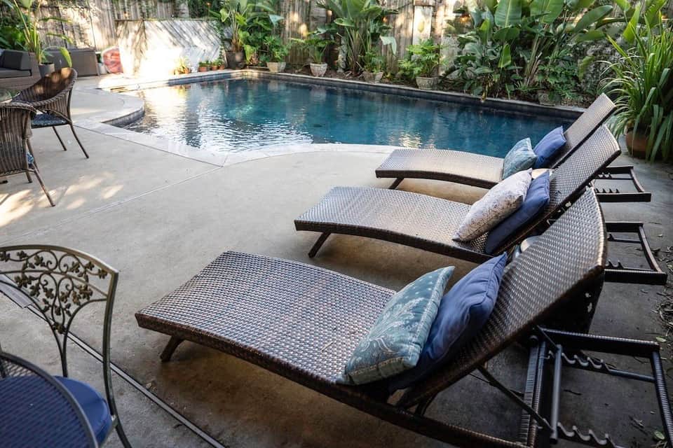 Luxury resort pool deck with loungers, cushions, and lush tropical vegetation surrounding blue water