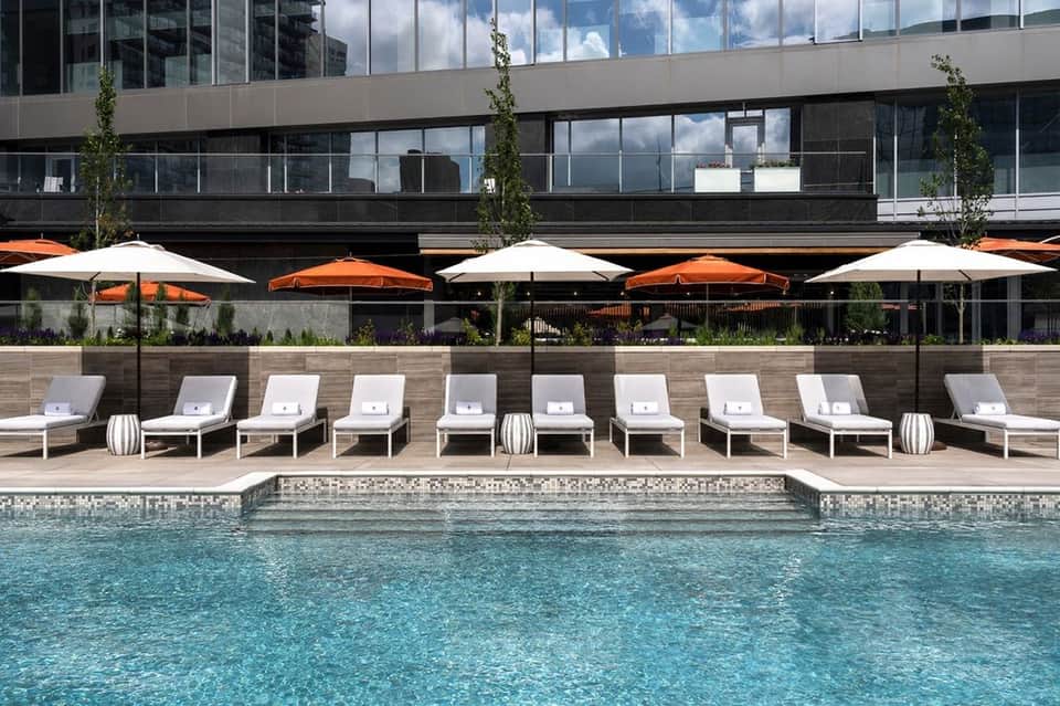 Resort pool with lounge chairs, alternating orange and white umbrellas, and modern building facade