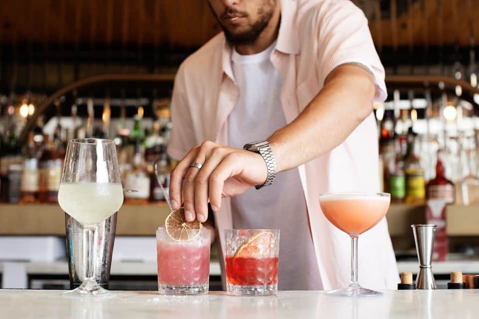 Bartender preparing colorful cocktails behind a bar counter with bottles in the background