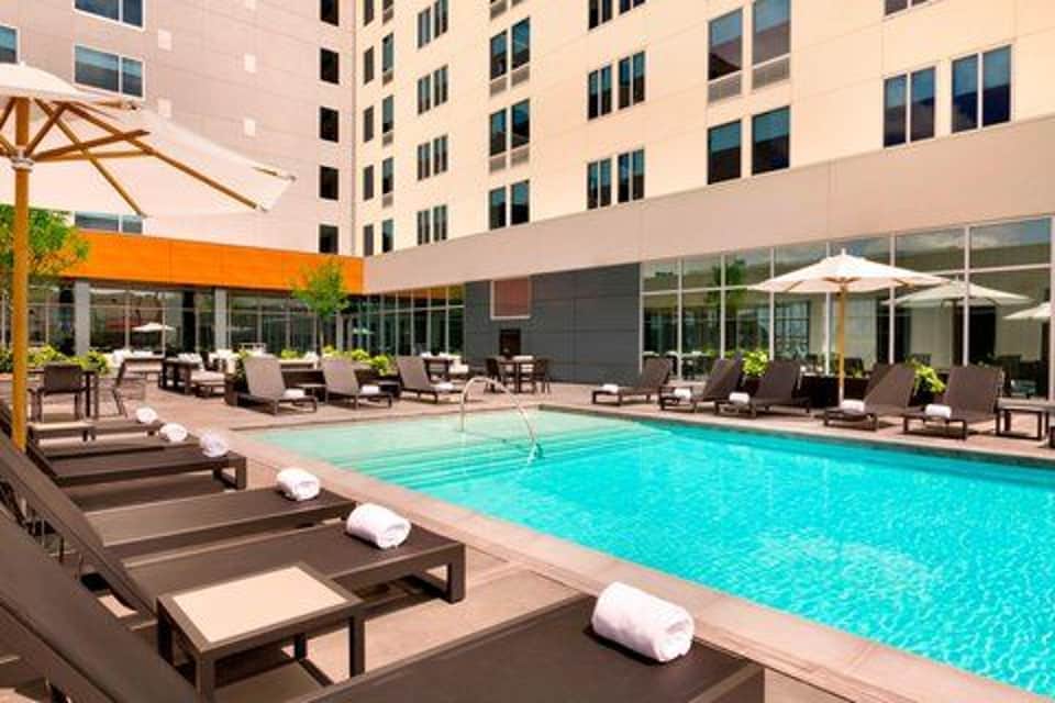 Outdoor resort pool with loungers, umbrellas, and multi-story building in bright daylight