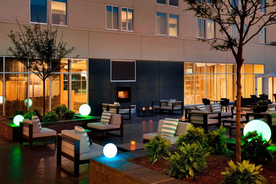 Courtyard lounge area at dusk with illuminated seating, fireplace, glowing sphere lights, and landscaping