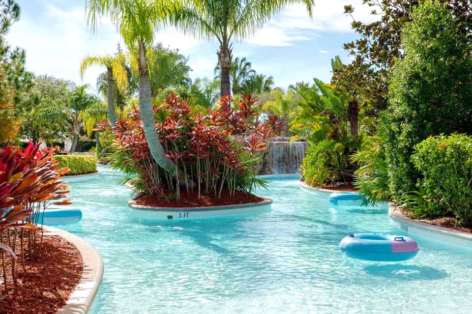 Tropical lazy river with turquoise water, palm trees, red flowers, and waterfall in resort setting