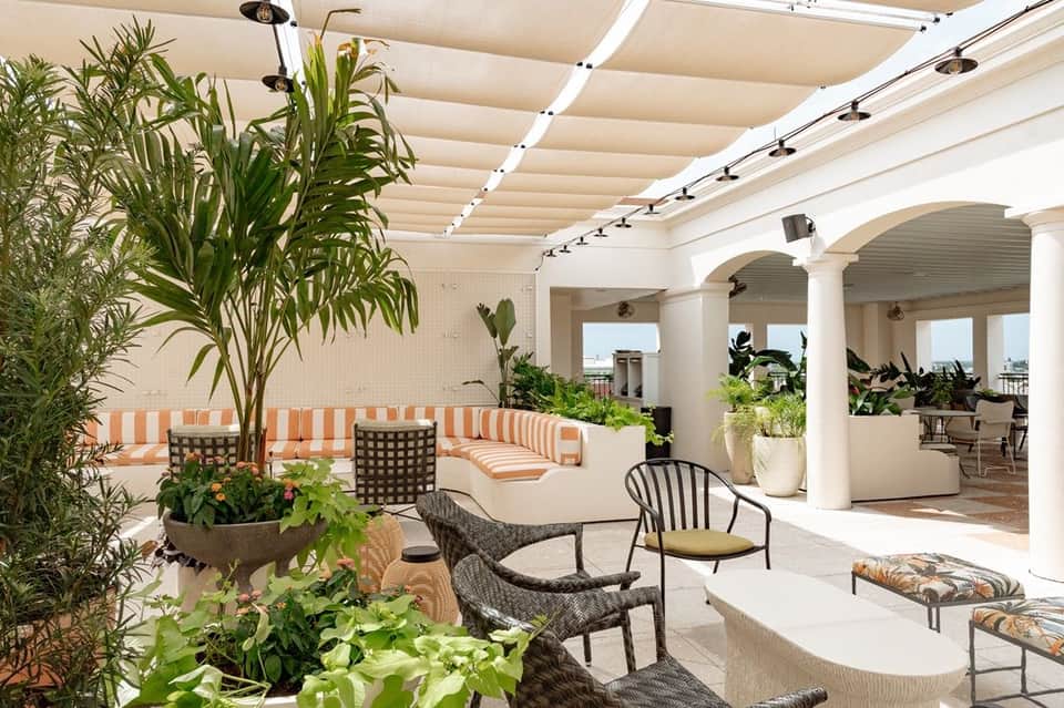 Rooftop patio with retractable shade system, striped seating, plants, and white pergola columns
