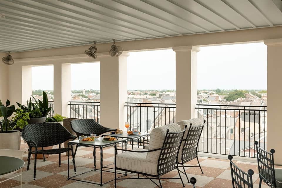 Rooftop terrace with metal pergola, black wicker chairs, dining table, and city skyline view