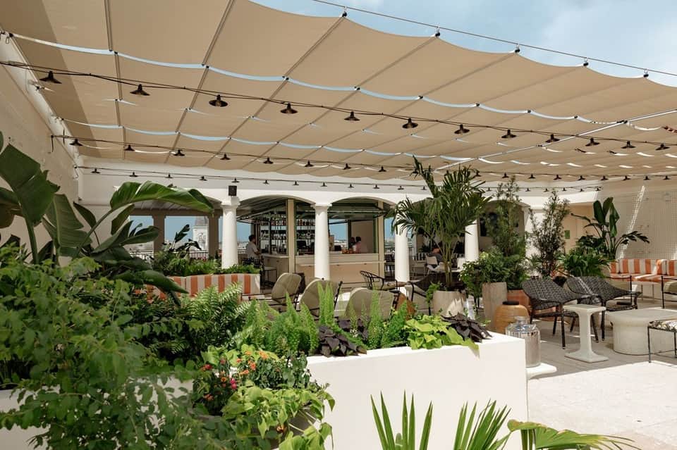 Elegant rooftop terrace with retractable shade sails, lush plants, bar area, and sea views