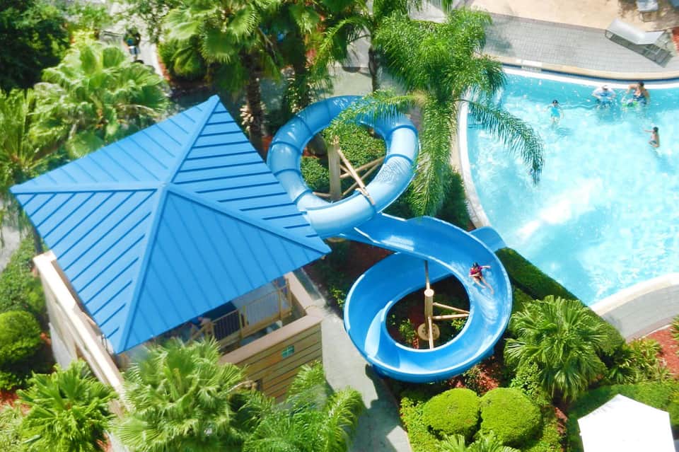 Blue water slide spiraling into resort pool surrounded by tropical palm trees
