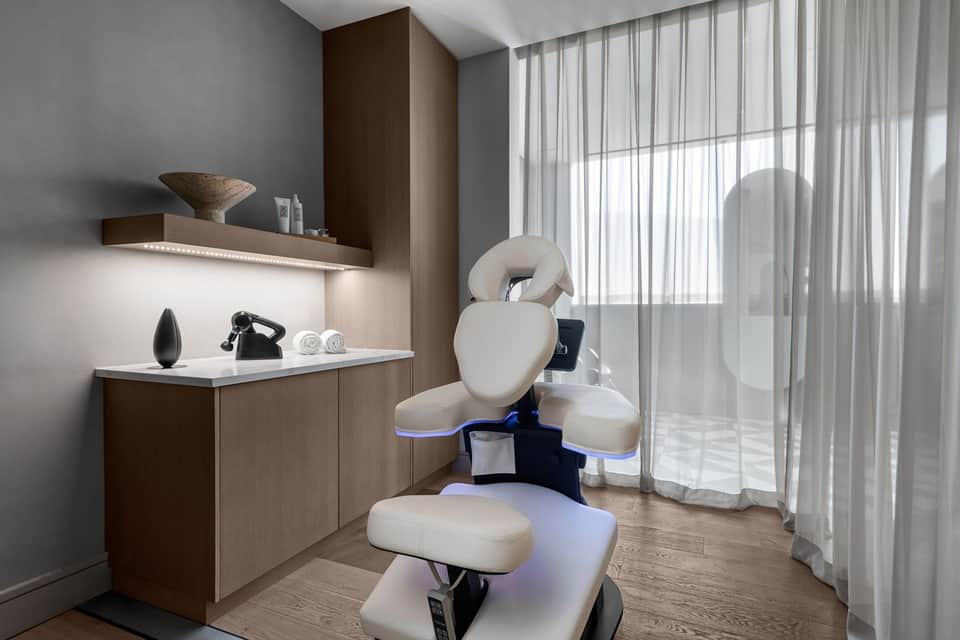 Professional spa treatment room with white massage chair, wooden cabinetry, and sheer curtains