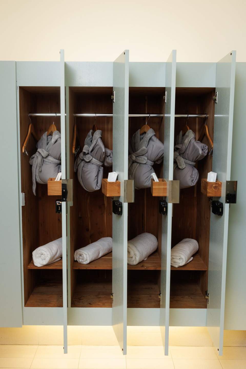 Individual locker storage with glass doors displaying gray robes and rolled white towels