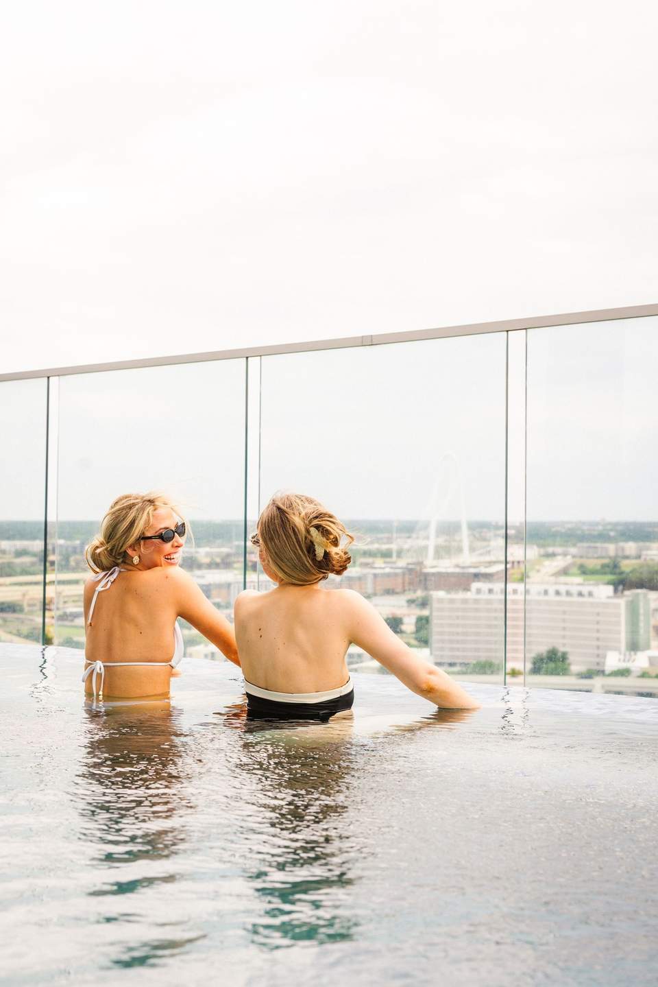 Two women in an infinity pool overlooking a cityscape from a high-rise hotel