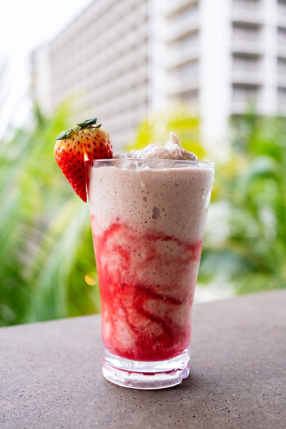 Strawberry garnished pink and white layered beverage with hotel towers in blurred background