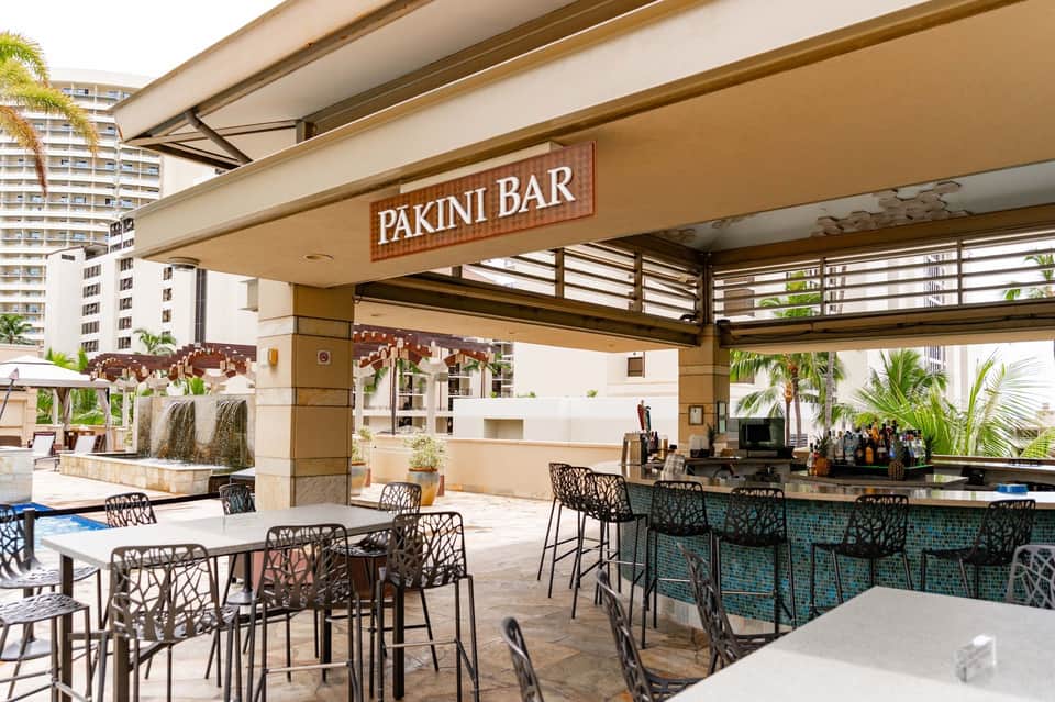 Pakini Bar outdoor seating area with black lattice chairs overlooking pool and palm trees