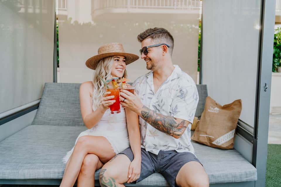 Couple toasting with tropical drinks on cushioned outdoor seating area