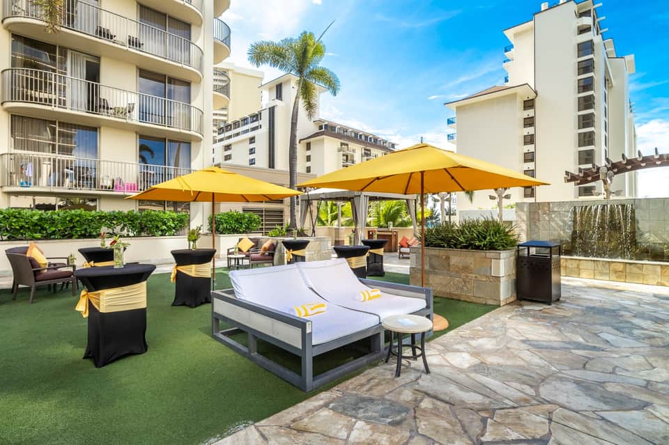 Luxury resort terrace with yellow umbrellas, lounge chairs, and apartment buildings under blue sky