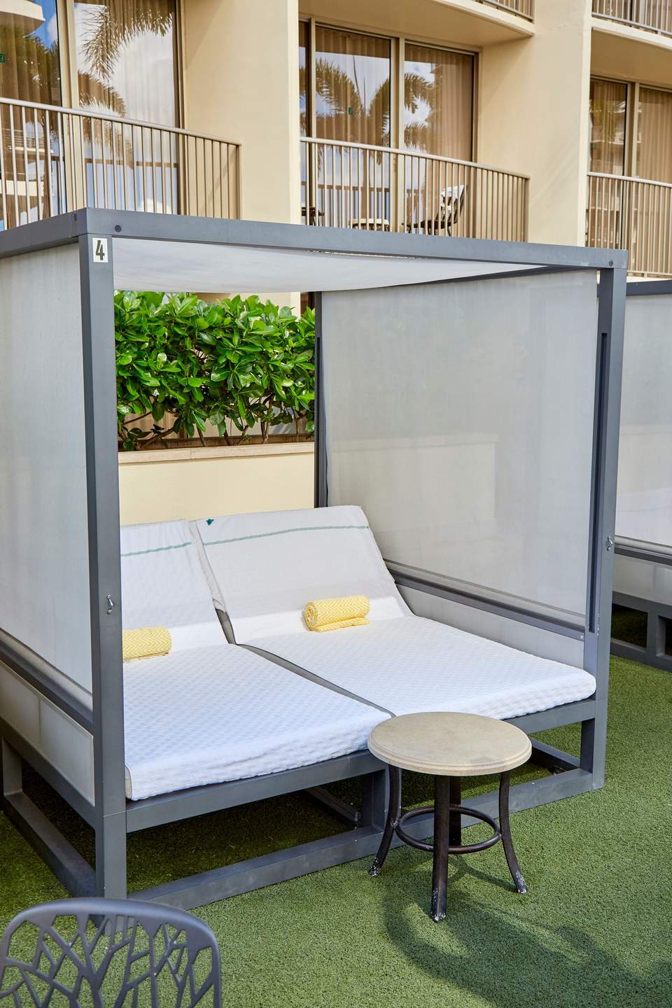 Modern gray daybed with white mattress and yellow pillows in private cabana with retractable screens
