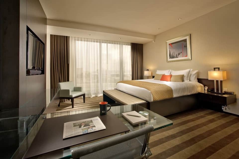 Luxury hotel bedroom with king bed, seating area, ocean view balcony, and warm lighting