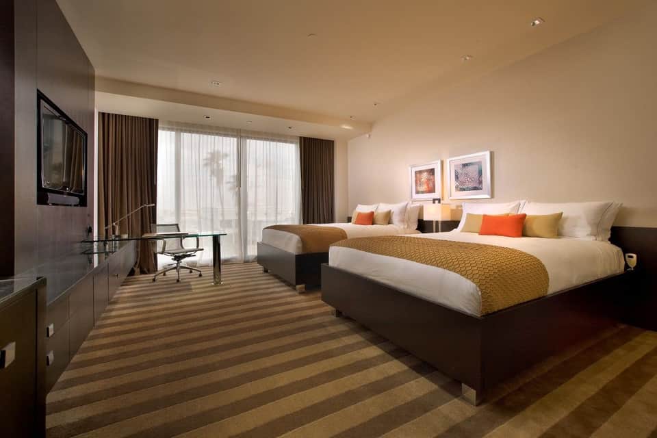 Luxury hotel room with two queen beds, gold accents, striped carpet, flat-screen TV, and panoramic balcony views