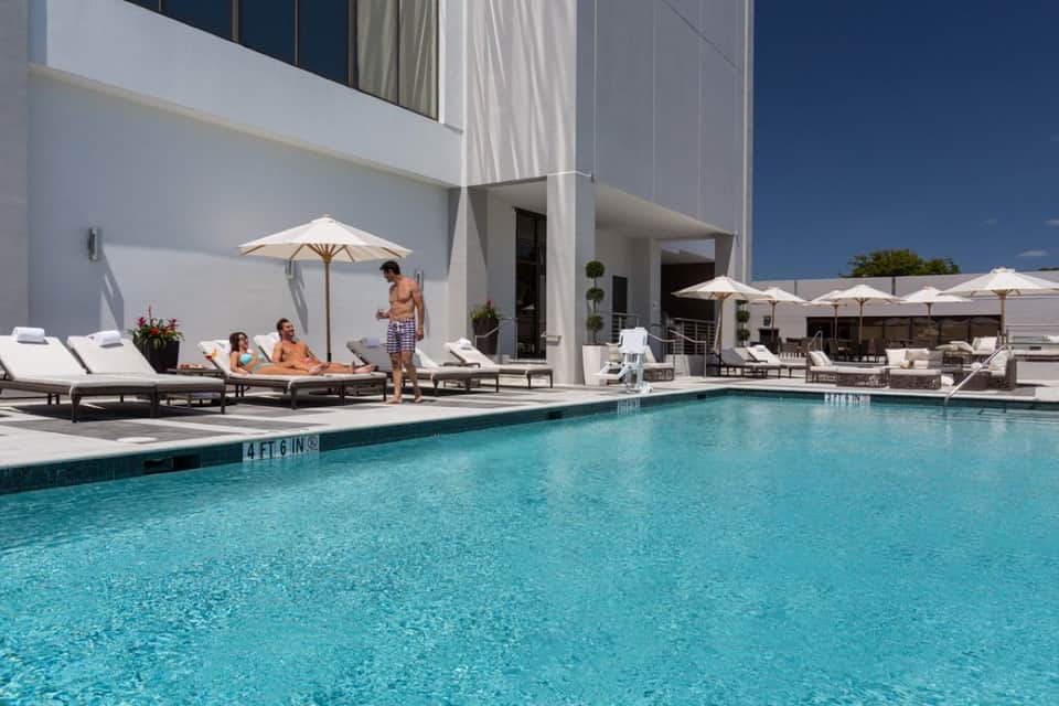 Resort pool deck with turquoise swimming pool, white loungers, umbrellas, and modern white building architecture