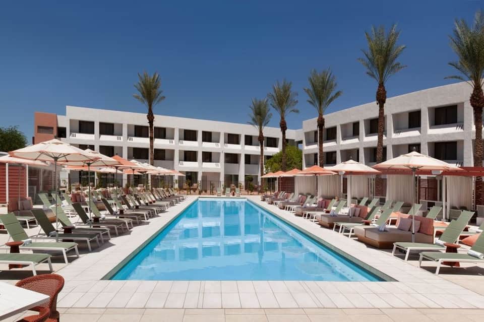 Resort pool with white umbrellas, lounge chairs, palm trees, and architecture