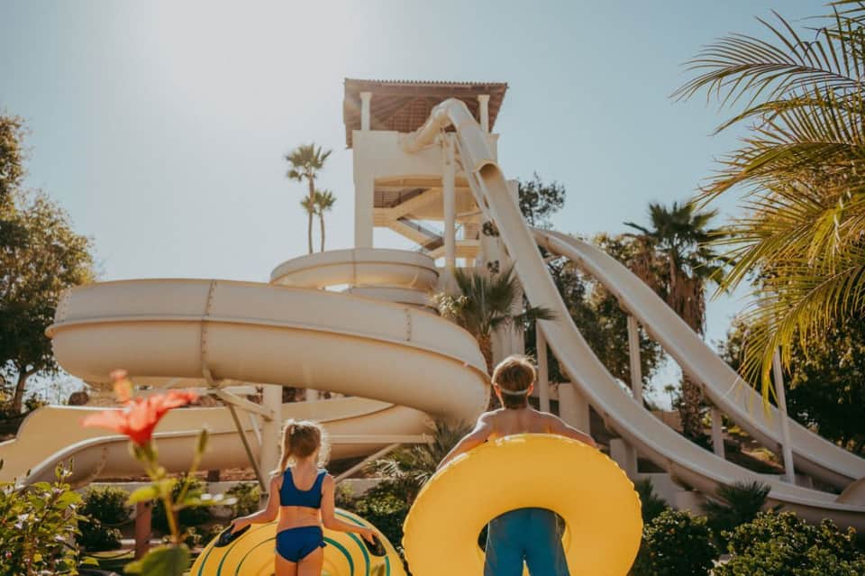 Children with yellow floats near water slides and palm trees at resort water park