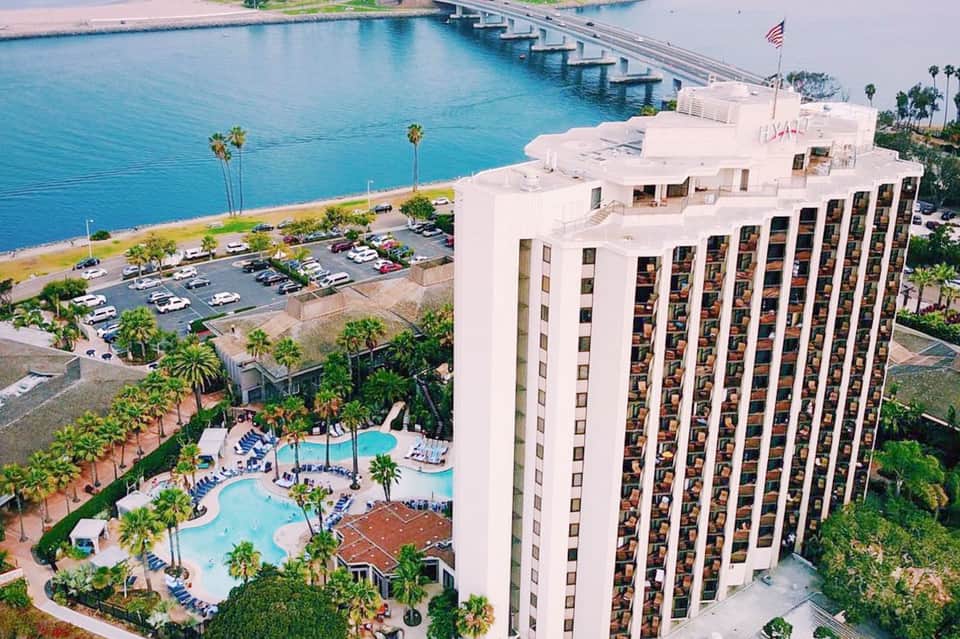 Waterfront high-rise hotel with curved white building and pool complex overlooking bay