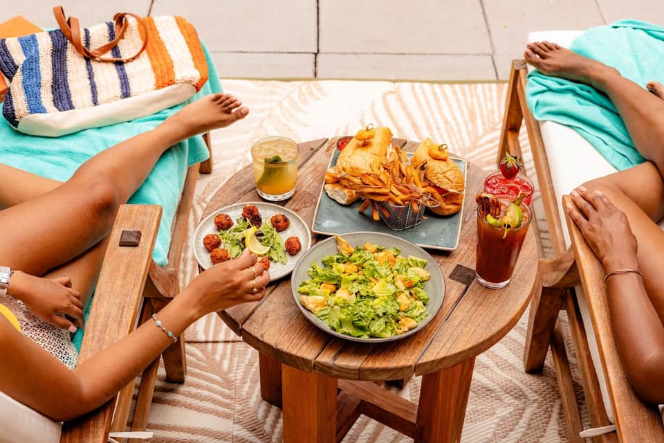Two people enjoying lunch at a wooden table with salads, fries, and beverages on a terrace