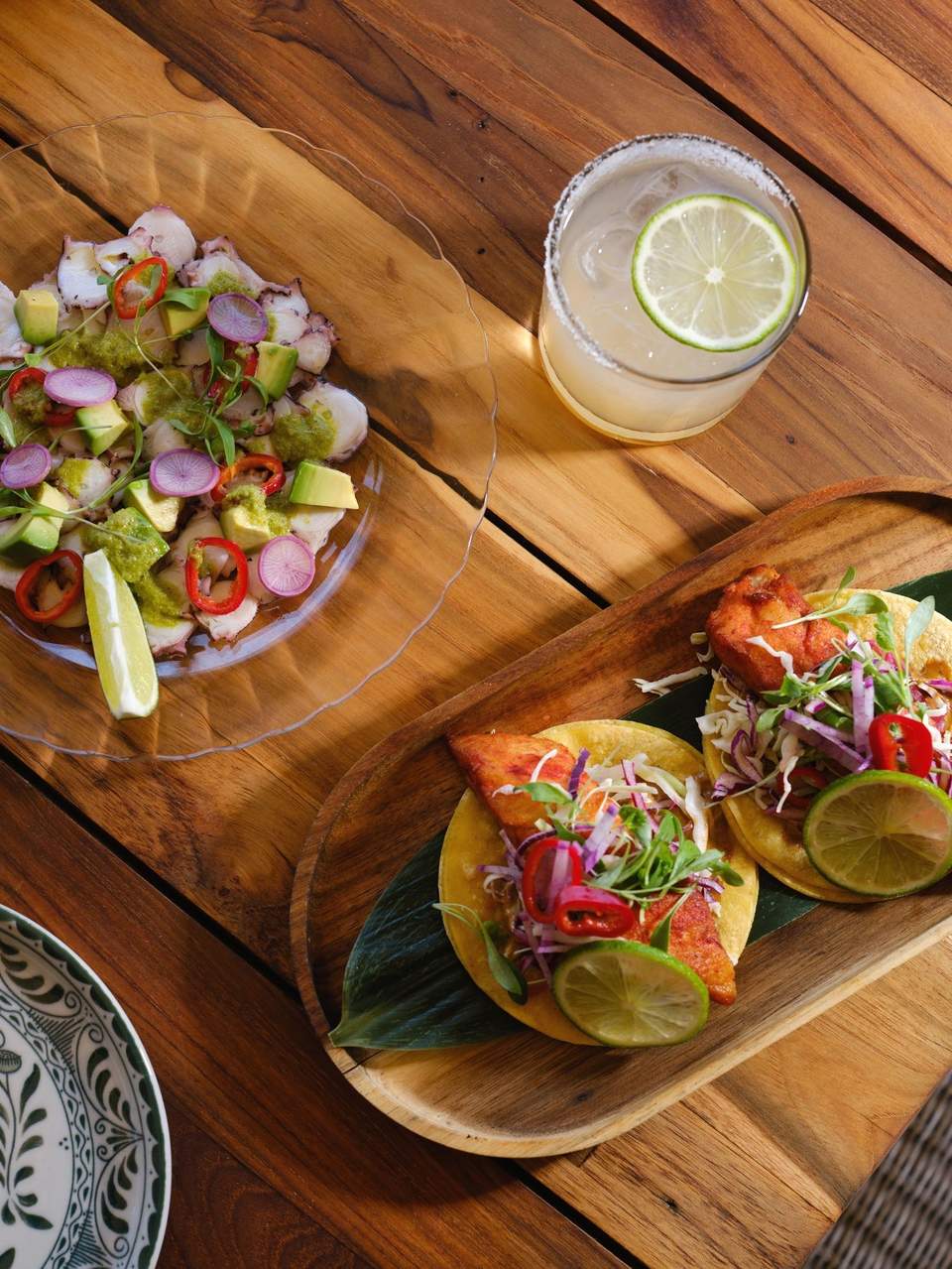 Fresh colorful salad, lime cocktail, and grilled fish tacos on wooden table in sunlight