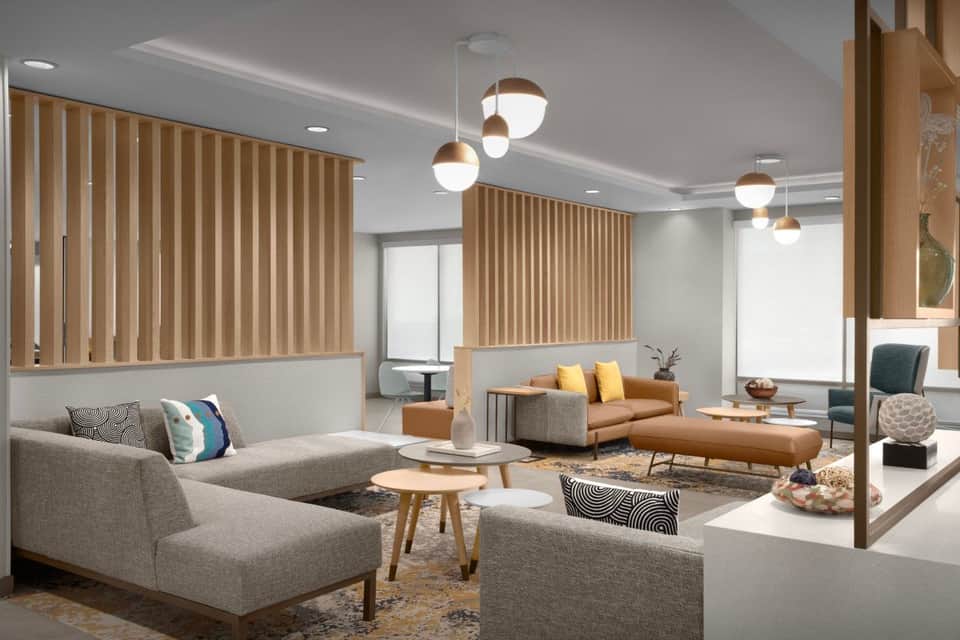 Modern hotel lobby lounge with gray upholstered seating, wooden accent walls, pendant lighting, and contemporary furnishings