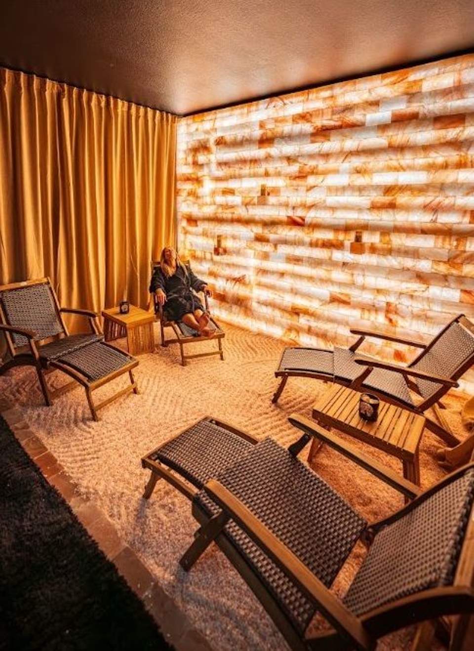 Salt therapy room with lounge chairs and glowing amber tile wall, creating a warm relaxing wellness space