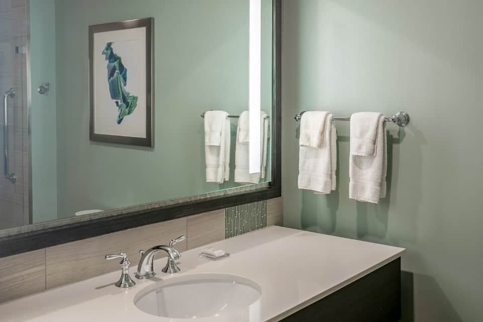 Spa bathroom with soft green walls, white sink, framed sailboat artwork, and chrome fixtures