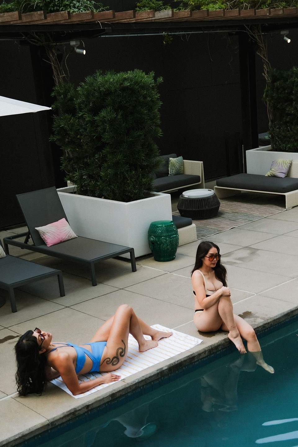 Two women relaxing on white towels by modern resort pool with lounge chairs