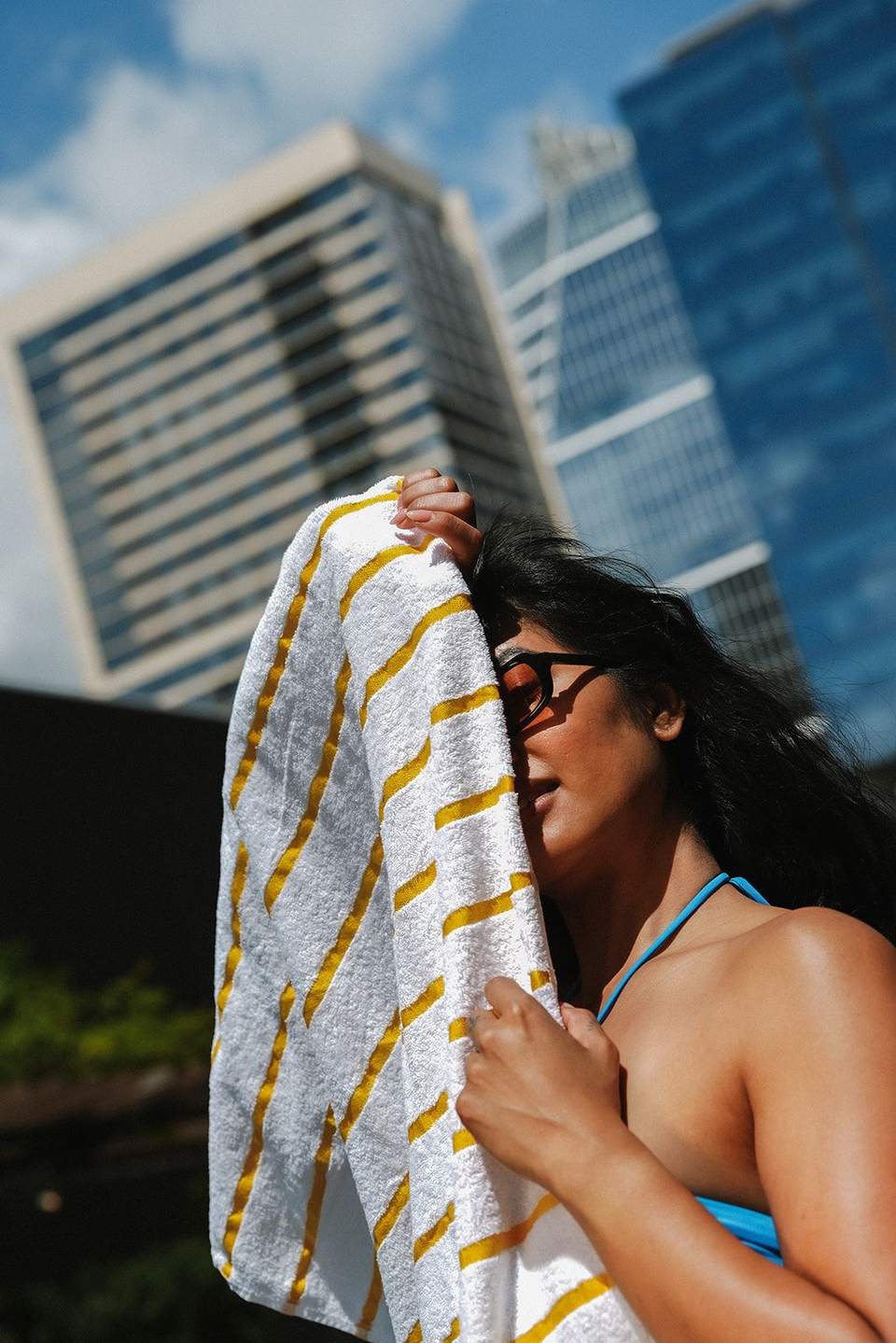 Woman in blue bikini holding striped towel with city buildings behind