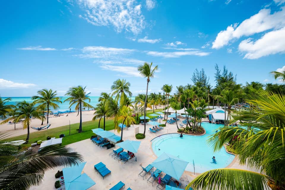 Aerial view of beachfront resort with pools, palm trees, and ocean