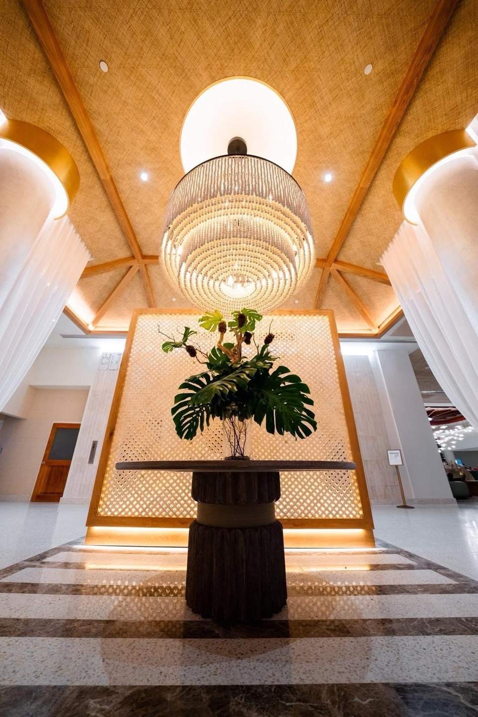 Luxurious lobby with geometric ceiling, central plant display, and warm lighting