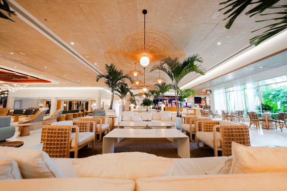 Modern lounge with woven wooden chairs, tropical plants, and expansive ceiling design