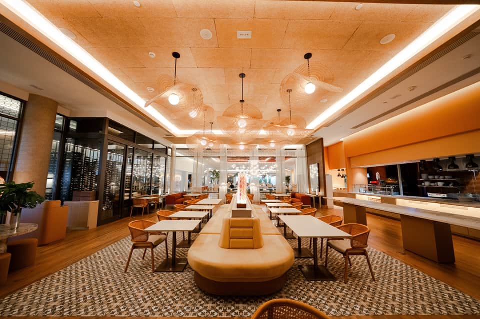 Modern hotel dining area with orange accents, wooden ceiling, pendant lights, and contemporary furniture