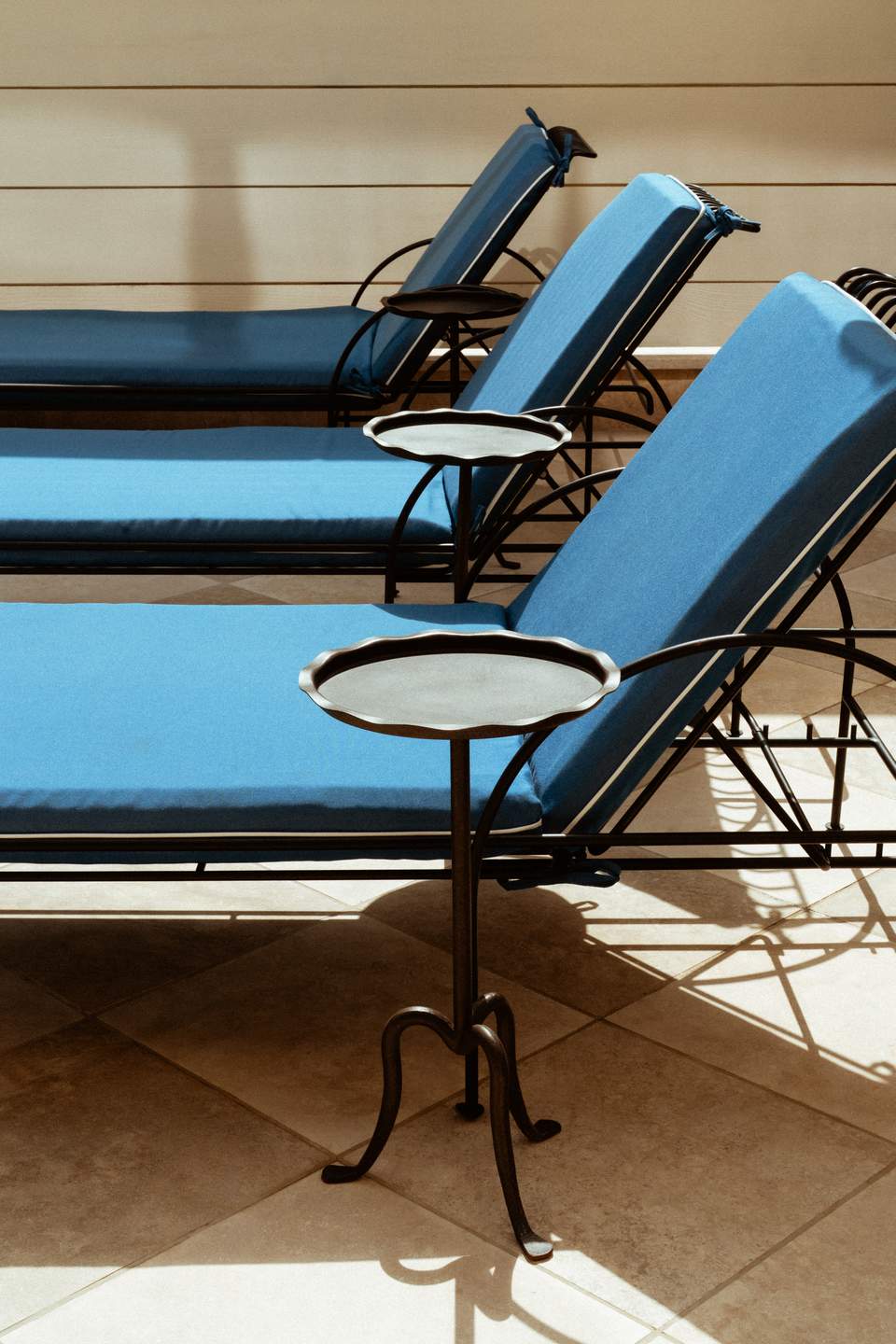 Row of blue cushioned lounge chairs with small round side tables on terrace