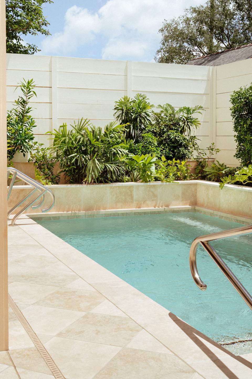 Rectangular swimming pool with turquoise water surrounded by white stone deck and tropical plants