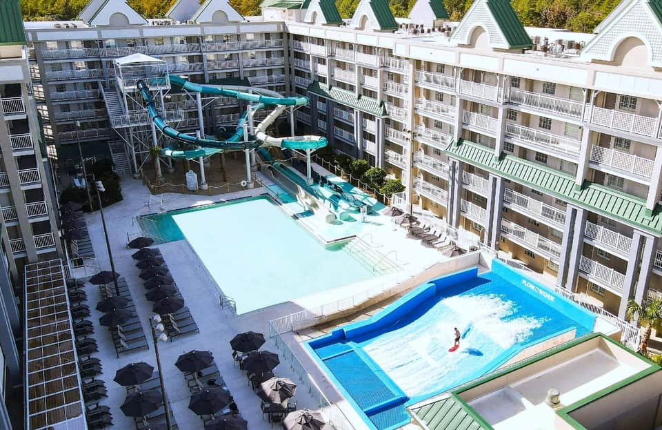 Aerial view of water park with turquoise slides, white swimming pool, black lounge chairs, and multi-story resort buildings