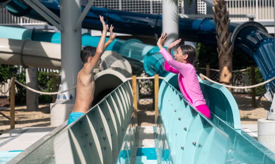 Two children jumping off waterslide platform into shallow water at resort pool area