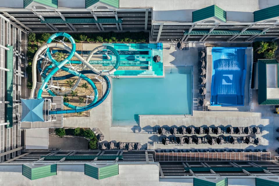 Overhead view of resort pool area with turquoise water slides, lounge chairs, and solar panel canopy
