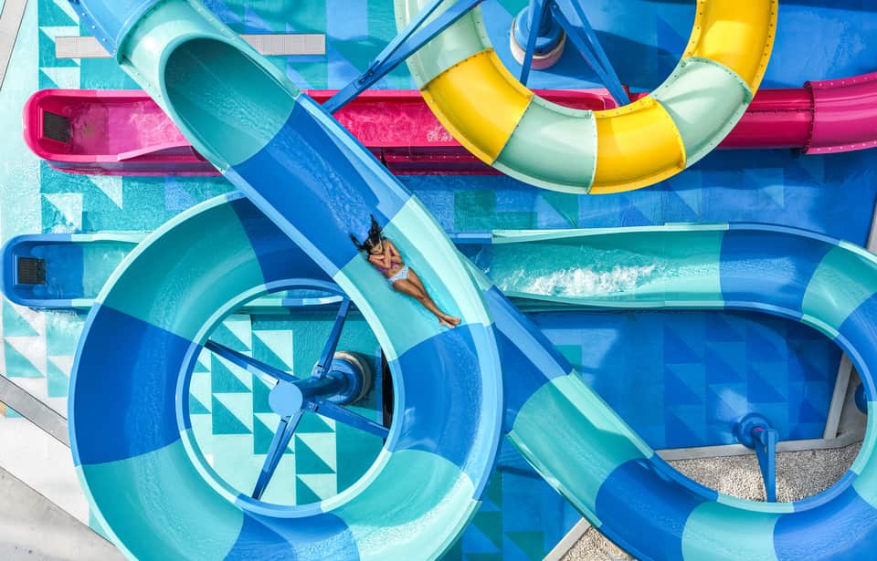Colorful tube water slides in bright pink, blue, yellow, and green with person sliding in turquoise water