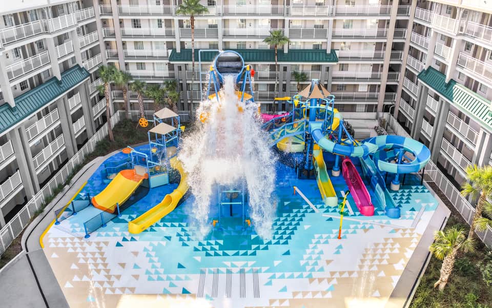 Aerial view of colorful water park with slides and splash pad surrounded by tall apartment buildings