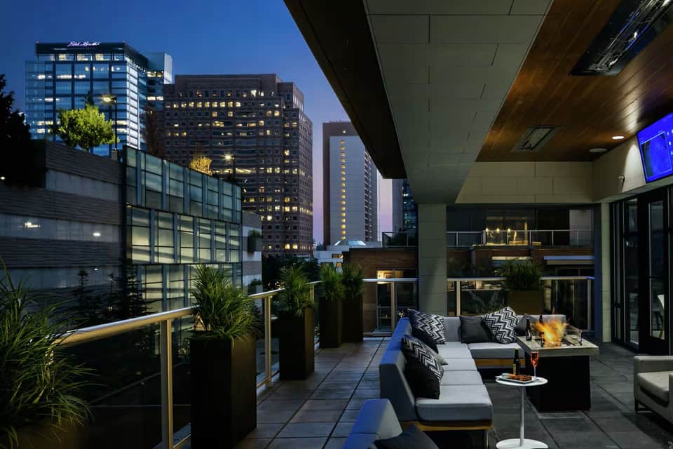 Hotel rooftop terrace at evening with fire pit, seating, city skyline view, and warm ambient lighting