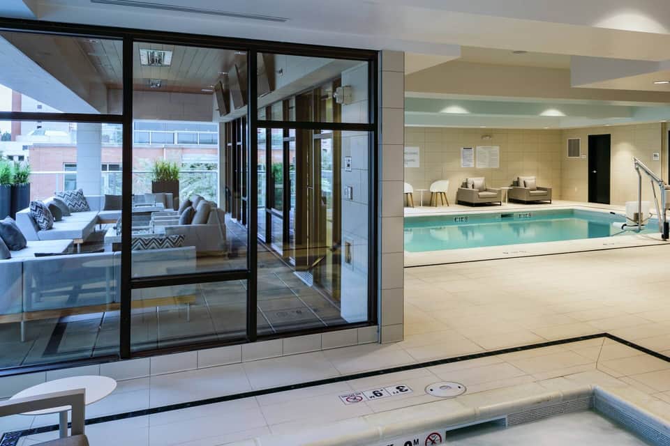 Indoor swimming pool with seating area and glass doors opening to outdoor terrace with lounge chairs
