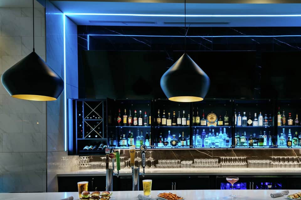Upscale bar with blue neon lighting, pendant lamps, backlit liquor bottles, and marble countertop