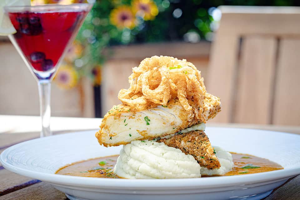 Gourmet plated dish with fried chicken, crispy noodles, and creamy sauce beside a red cocktail