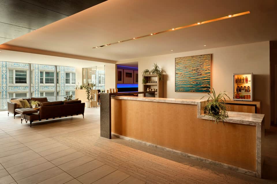 Modern hotel lobby with reception desk, lounge seating, and city views through floor-to-ceiling windows