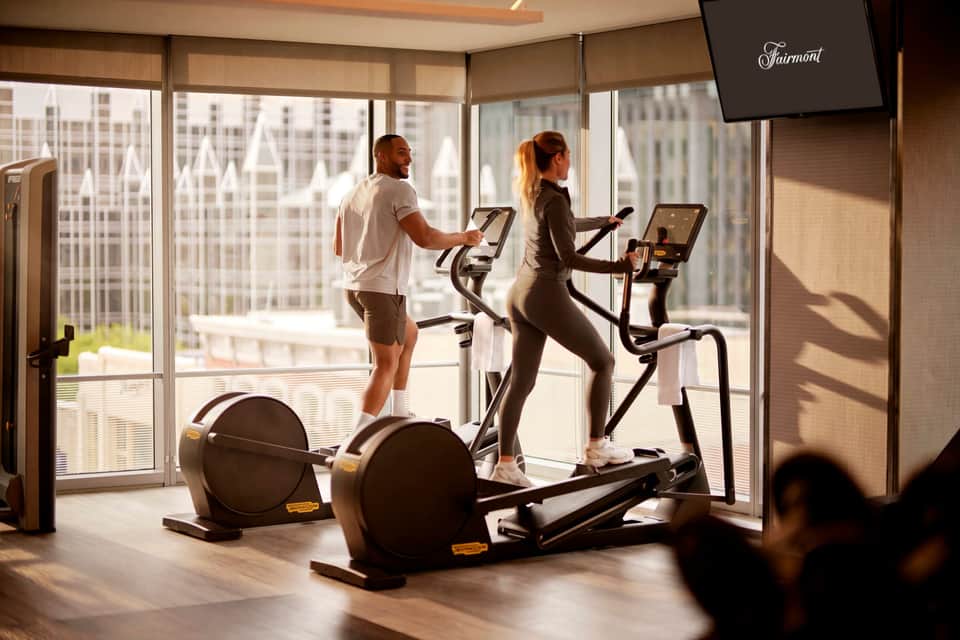 Fitness center with two people on stationary bikes overlooking city skyline through floor-to-ceiling windows