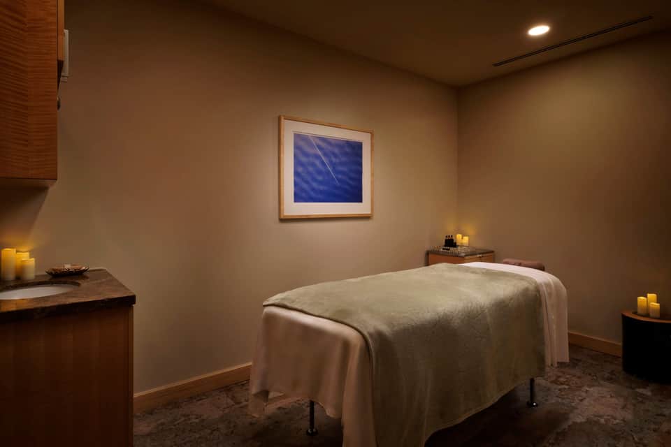 Spa treatment room with massage table, calming blue artwork, and warm ambient lighting