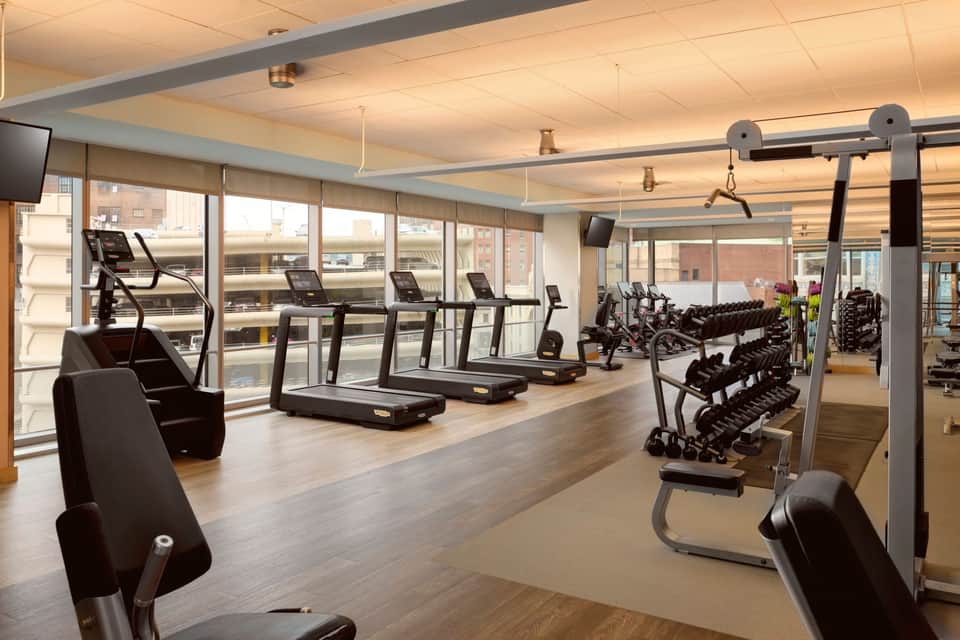 Spacious gym with cardio equipment, free weights, mirrors, and natural light from floor-to-ceiling windows